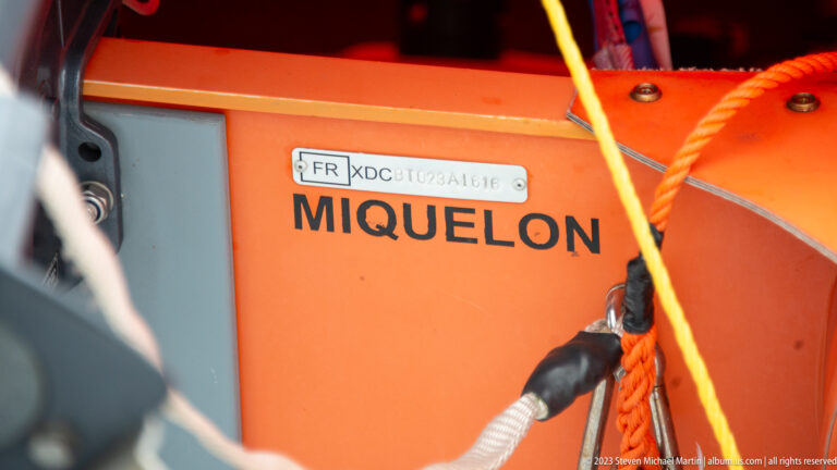 Close view of an orange Miquelon-marked lifebuoy with ropes, fittings, and a small French registration plate.