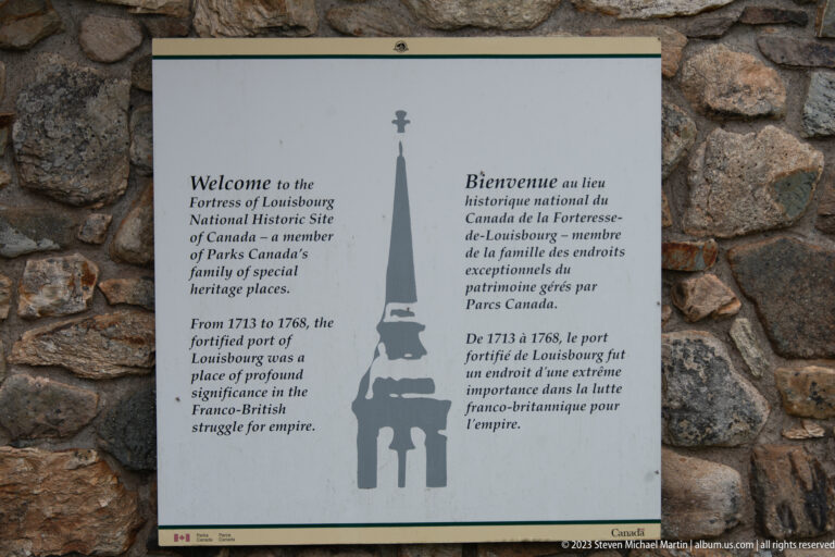 Bilingual welcome panel for Fortress of Louisbourg mounted on a rough stone wall.