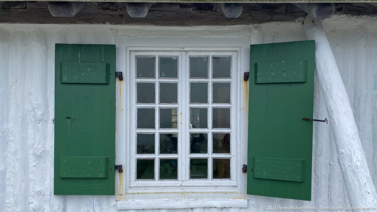 White multi-pane window with dark green shutters set into a thick whitewashed wall.