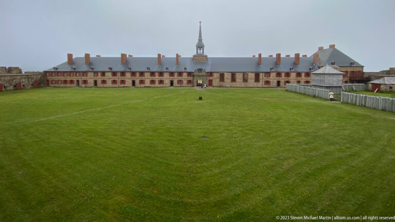 Wide grassy parade ground facing long red-trimmed barracks with a central chapel spire.