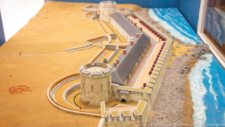 Scale model of a long waterfront fortification with a prominent round tower and curved defenses.