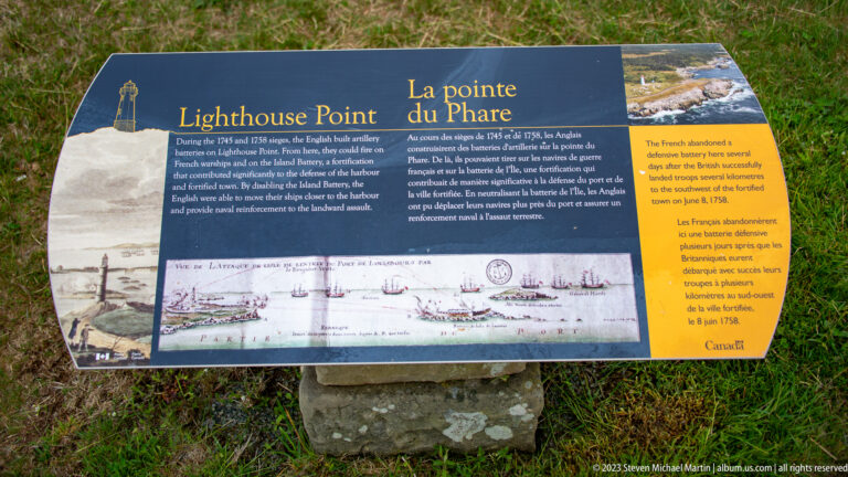 Bilingual Lighthouse Point interpretive sign with historic illustrations, map, photographs, and explanatory text on a grassy site.