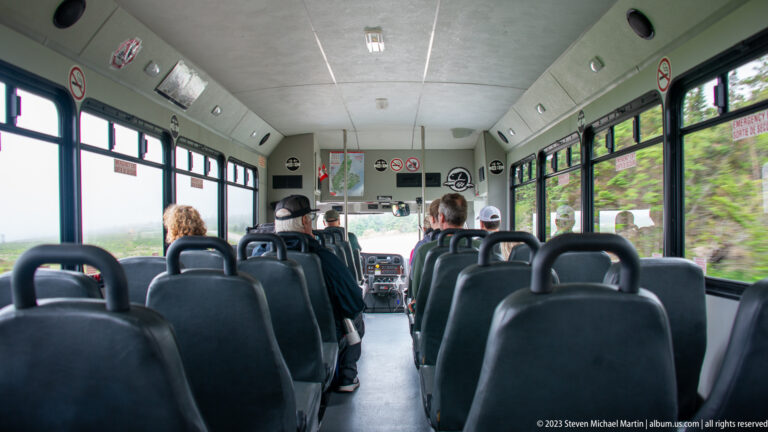 Interior of a visitor shuttle bus with rows of dark seats and passengers near the front.