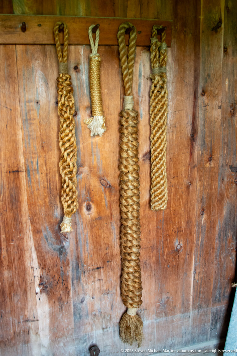 Several knotted and tightly wrapped rope samples hanging on a wooden wall.