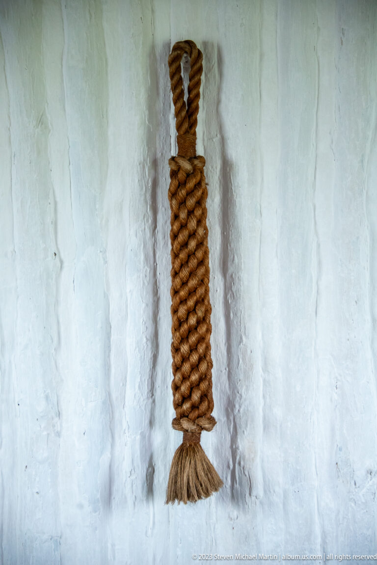 Single tightly wrapped cylindrical ropework piece with top loop and loose fibers at bottom.