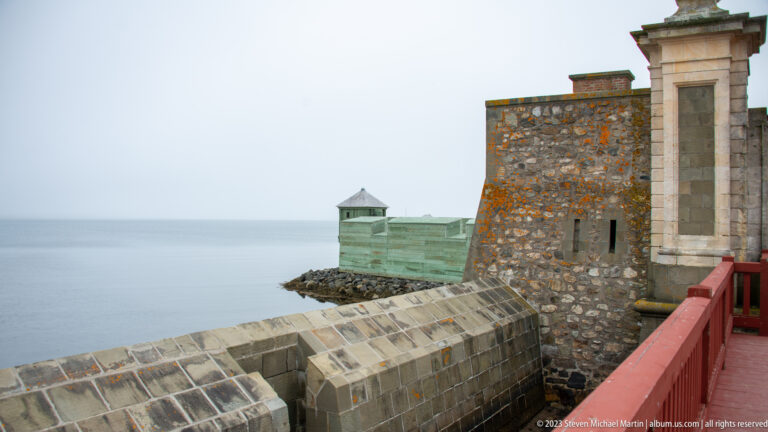 Stone fortress wall and angular revetments beside calm water, with a small roofed sentry box projecting near the shore.
