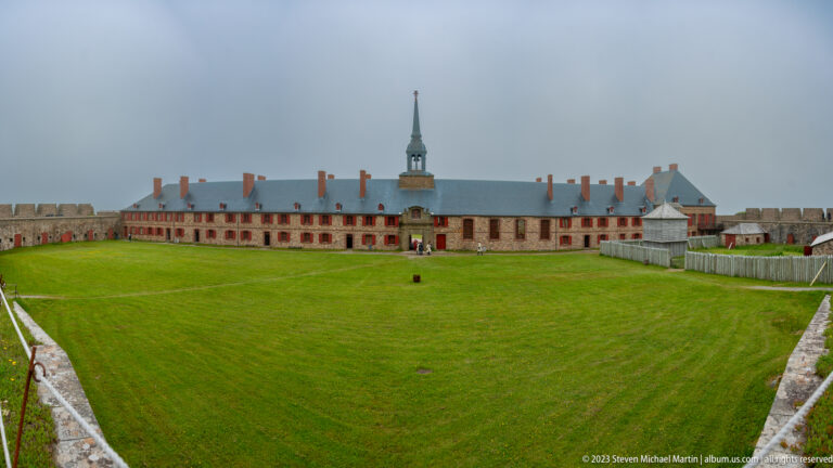 Wide grassy courtyard enclosed by fortress walls, facing the long King’s Bastion barracks and chapel tower.