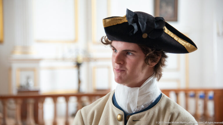 Close portrait of a young interpreter in a black gold-trimmed tricorn hat and pale period coat.