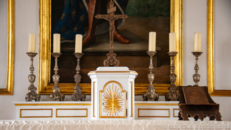 White and gold tabernacle, crucifix, and six ornate candlesticks arranged across the chapel altar.