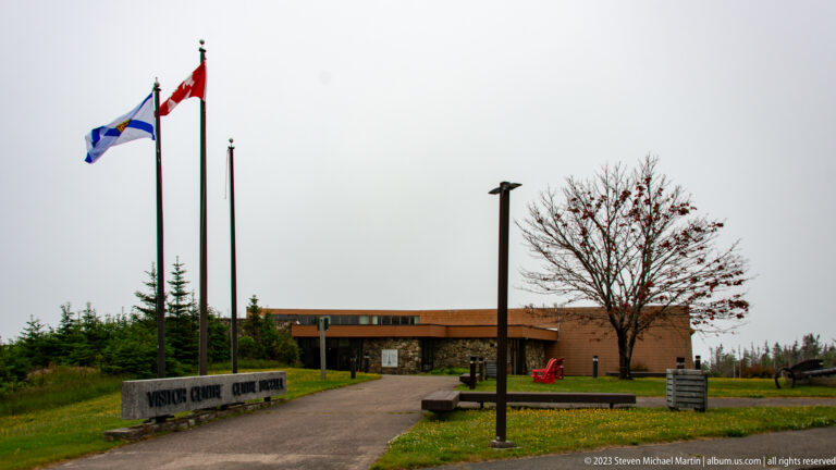 Visitor Centre forecourt with Canadian and Nova Scotia flags, benches, and a leafless tree.