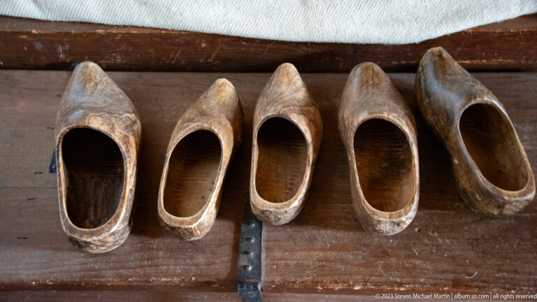 Five worn wooden shoes arranged in a row on a dark plank beneath a bunk.