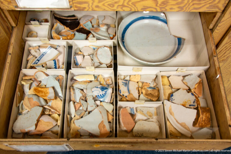 Boxes filled with ceramic sherds beside a partially reconstructed white vessel with blue painted decoration.