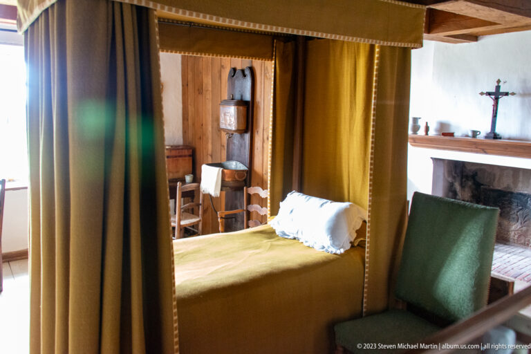 Mustard canopied bed, green chair, fireplace, and wooden furnishings in a reconstructed eighteenth-century bedchamber.