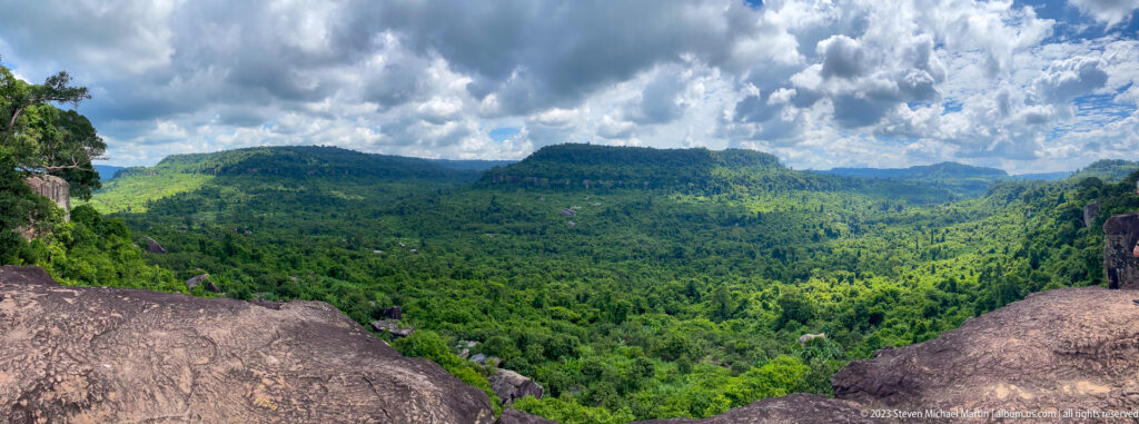 Wide green valley between dark rock outcrops beneath dramatic cumulus clouds.
