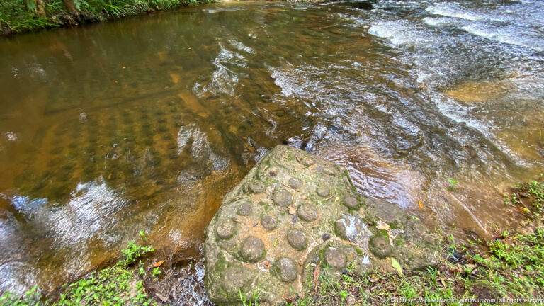 Triangular carved sandstone slab projects into shallow flowing water.