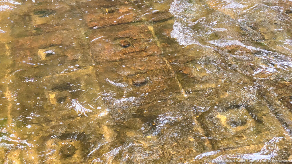 Square geometric stone carving visible beneath shallow rippling river water.