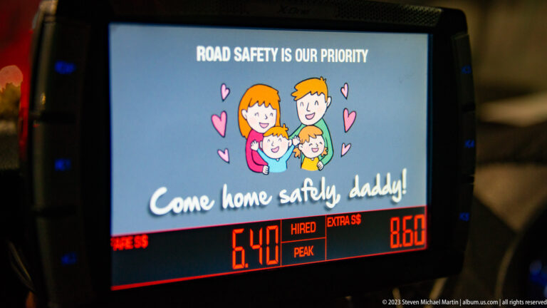 Taxi meter and digital screen showing a family illustration, road-safety message, and illuminated fare figures.