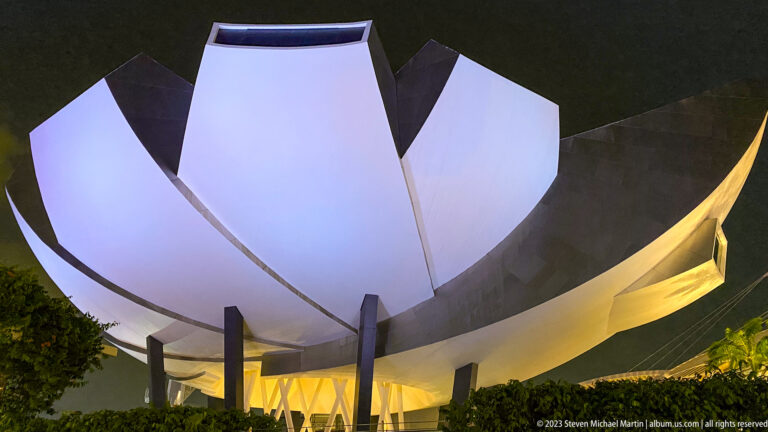 Low-angle nighttime view of the white ArtScience Museum petals above dark supports.