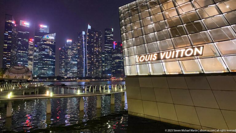 Louis Vuitton pavilion with illuminated sign beside Marina Bay and the downtown skyline.