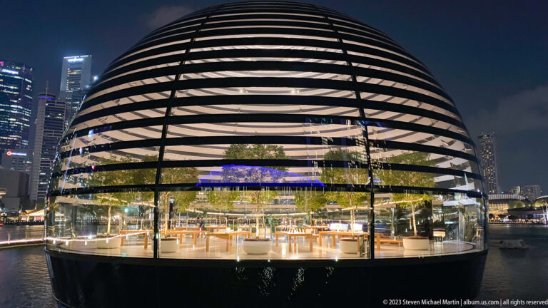 Frontal view of the banded spherical Apple pavilion with a glowing glass interior.