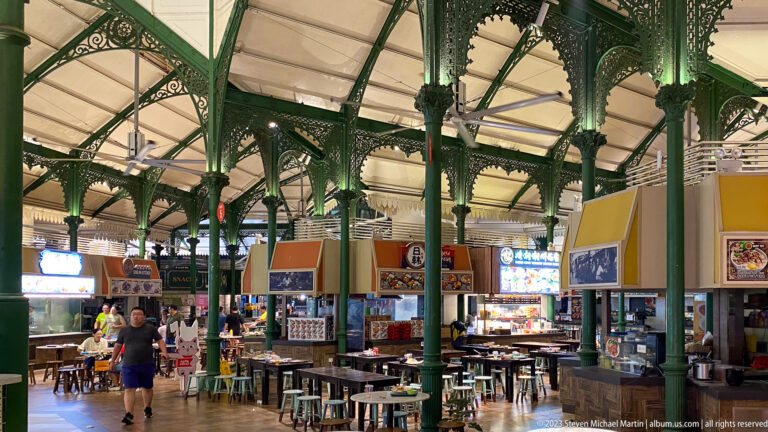 Broad Lau Pa Sat interior with green iron columns, hawker stalls, tables, and a few diners.