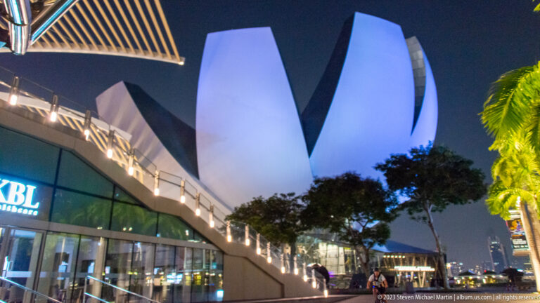 White petal-shaped ArtScience Museum above a sloping, illuminated promenade at night.