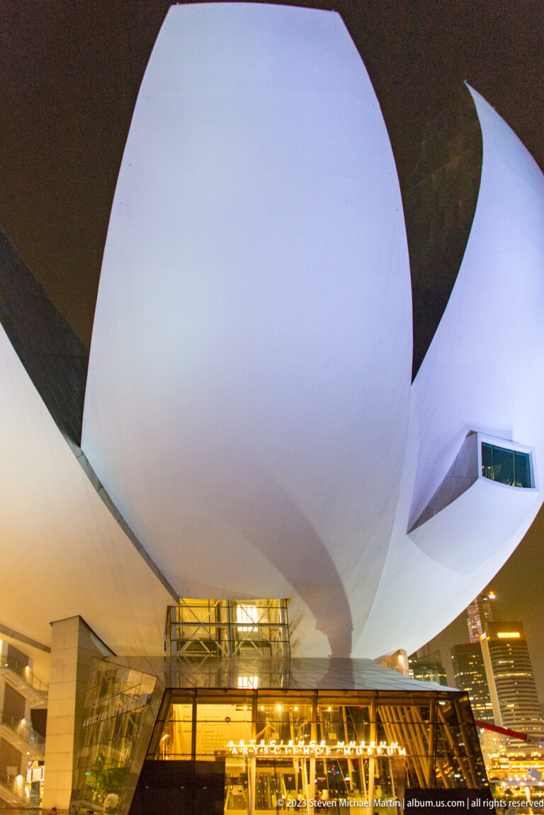 Close view of glowing white ArtScience Museum petals above a glass entrance at night.