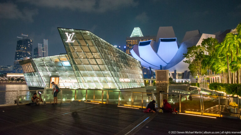 Illuminated Louis Vuitton pavilion with the white ArtScience Museum rising behind it at night.
