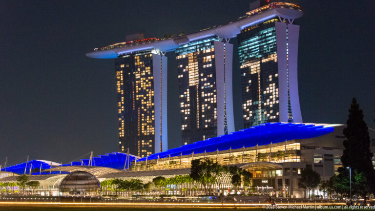 Marina Bay Sands at night above a long blue-lit waterfront canopy.