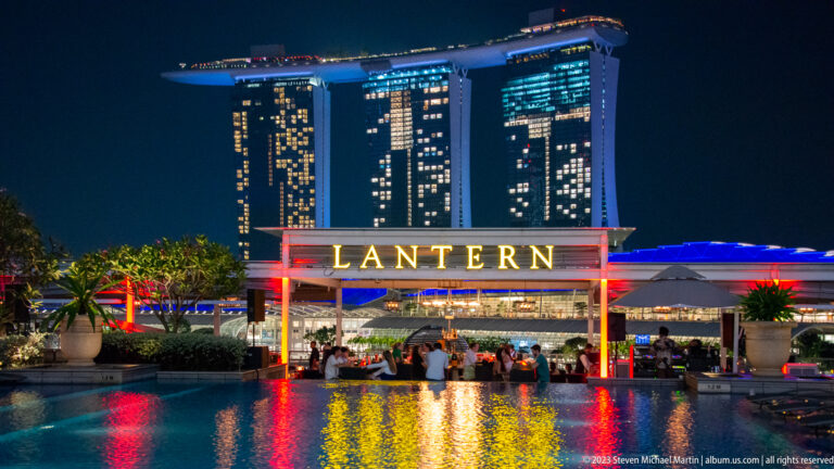 Lantern bar sign above a pool, with Marina Bay Sands illuminated in the background.