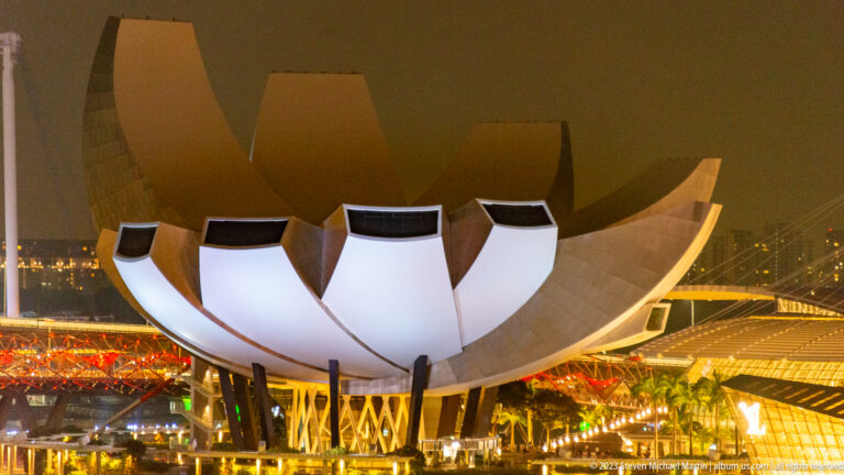 Close nighttime view of the illuminated ArtScience Museum with red-lit bridge structures behind.