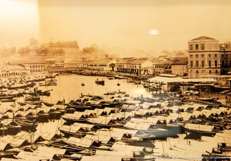 Sepia historic harbor scene with many small boats and colonial waterfront buildings.