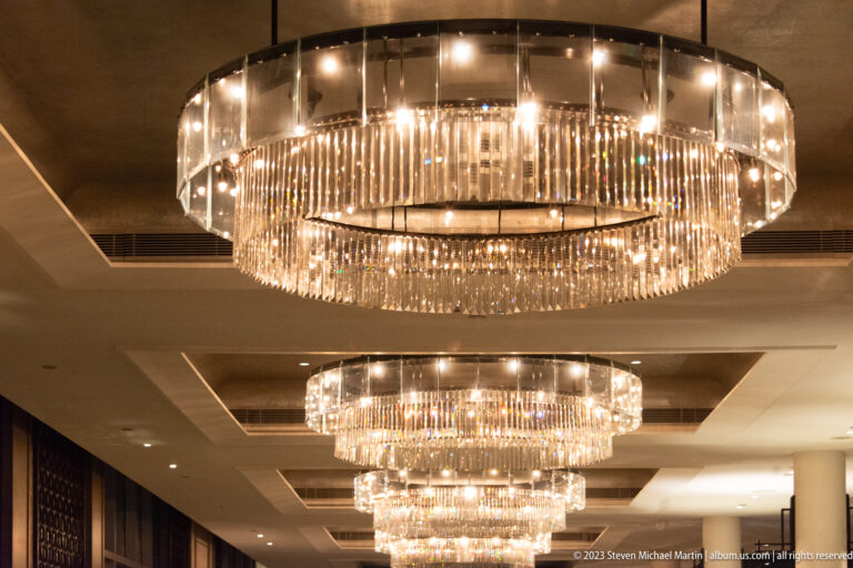 Multiple circular crystal chandeliers hanging in a row beneath a coffered ceiling.