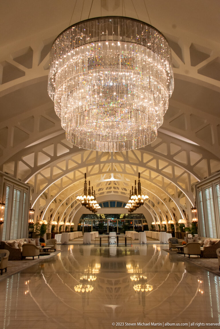 Large crystal chandelier above a polished hotel lobby with white vaulted arches and symmetrical seating.