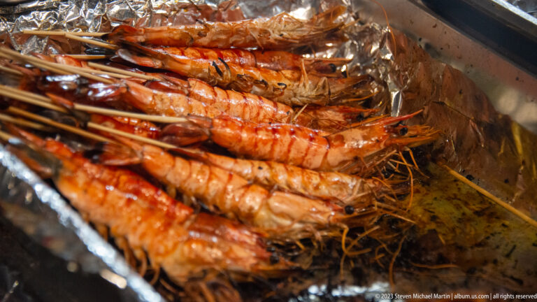 Close view of seasoned whole prawns grilling on a metal cooking surface.