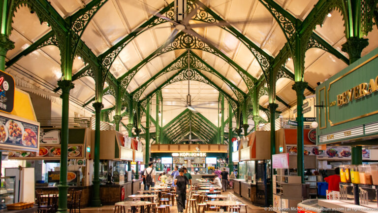 Long interior of Lau Pa Sat with green cast-iron columns, food stalls, and dining tables.