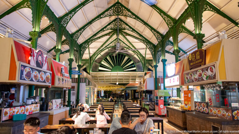 Food stalls and diners beneath green cast-iron arches inside Lau Pa Sat.