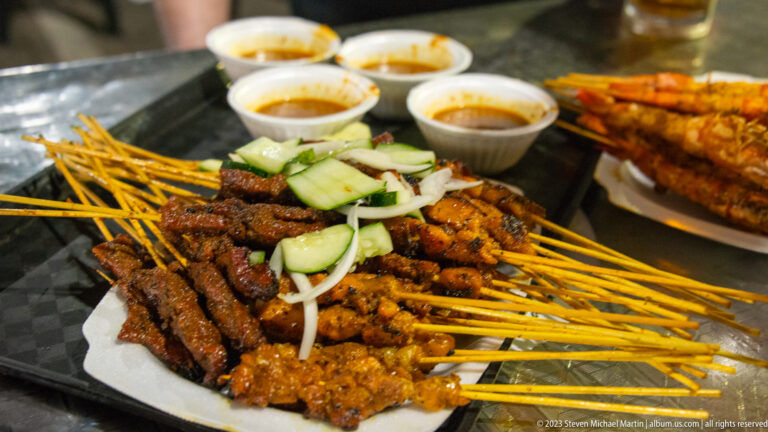 Large platter of mixed satay skewers with cucumber, onion, and dipping sauces.
