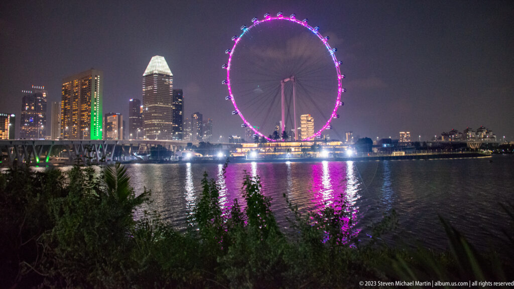 Magenta-lit Singapore Flyer and matching reflections across Marina Bay at night.