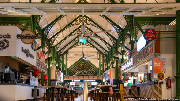 Nearly empty Lau Pa Sat aisle with green iron arches, food stalls, and high tables.
