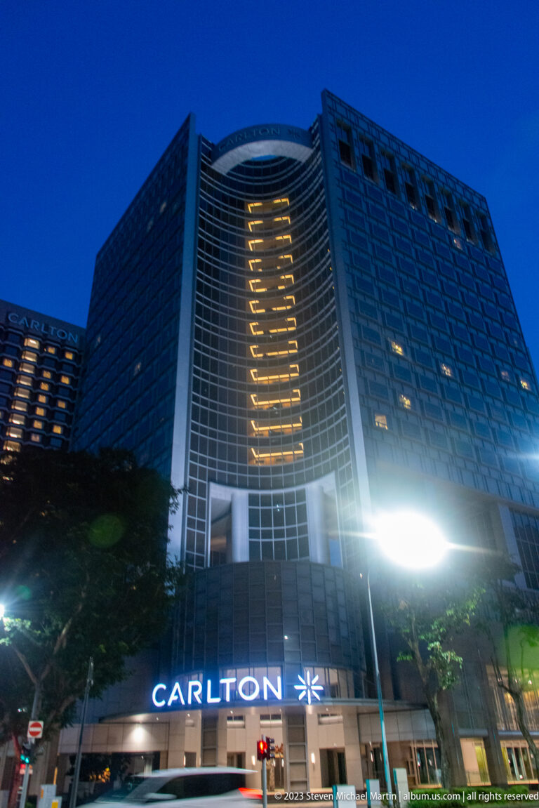 Low-angle nighttime view of the Carlton Hotel with illuminated central windows and entrance sign.