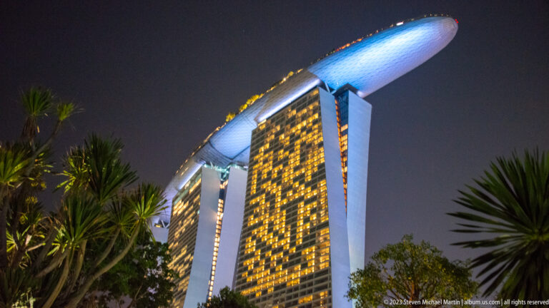 Low-angle nighttime view of Marina Bay Sands, with palm fronds around the three towers and rooftop SkyPark.