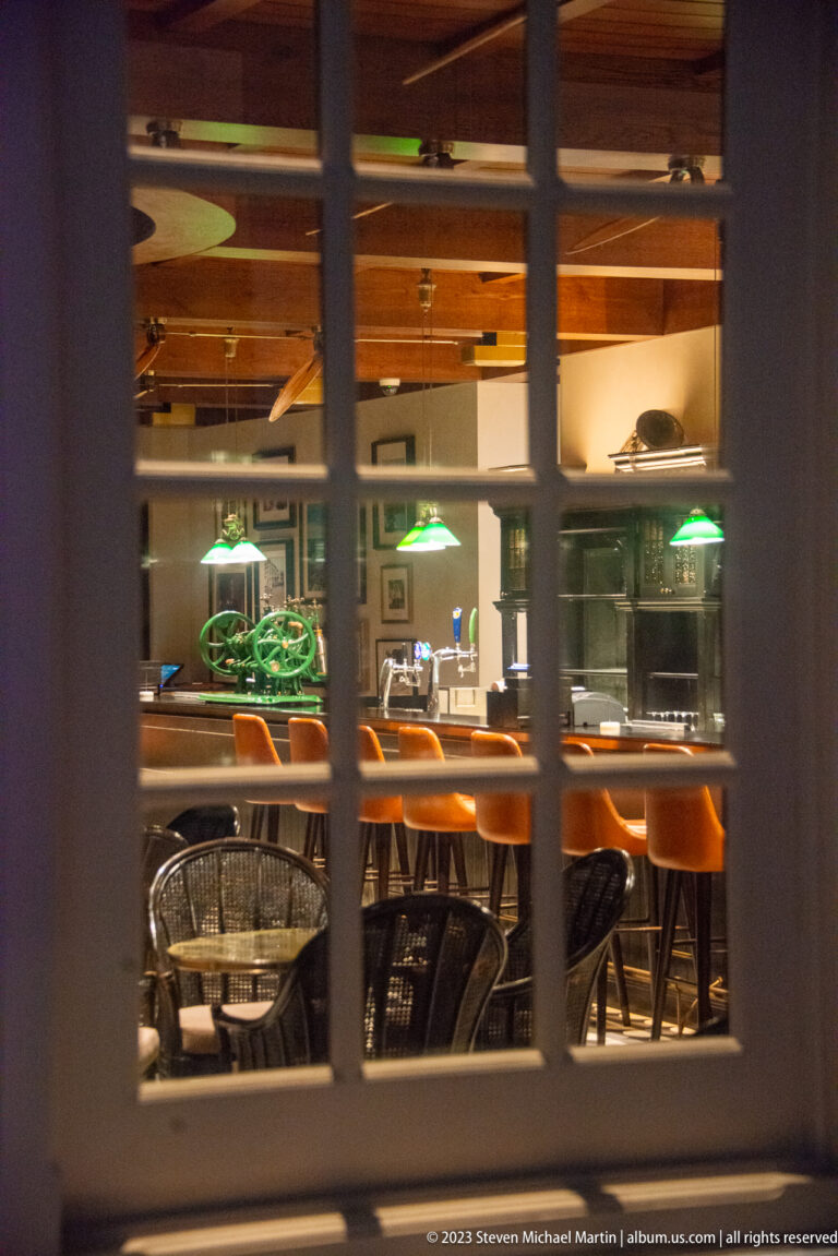 Long Bar interior viewed through window panes, with orange stools, tables, and green lamps.
