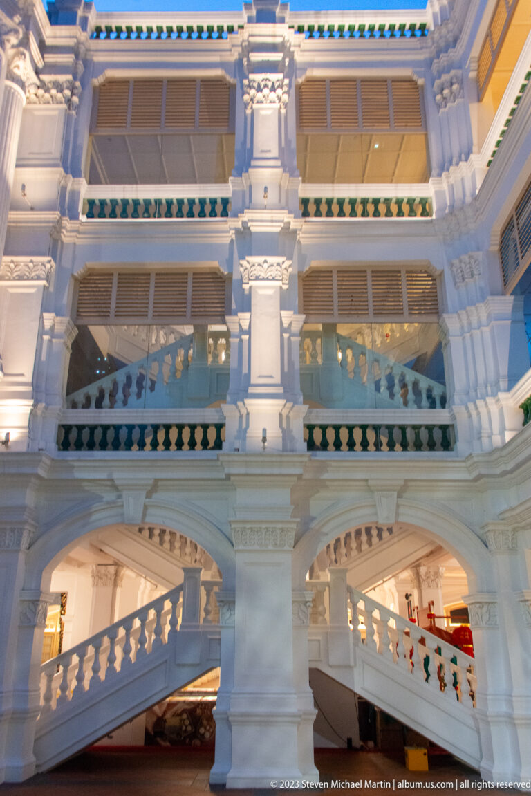 White multi-level courtyard with arcades, balustrades, shutters, and staircases at Raffles Singapore.