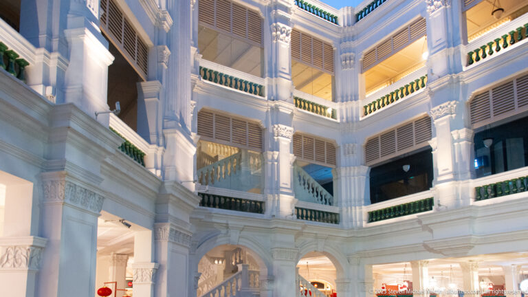 Corner view of white arcades, shutters, balconies, and stairs inside Raffles Singapore.