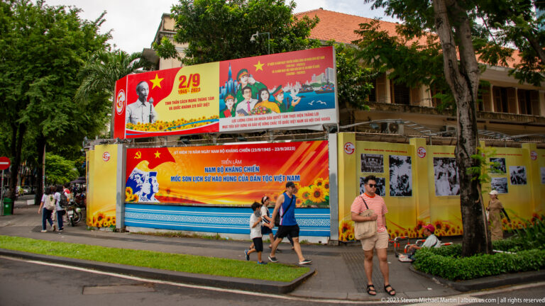 Red-and-yellow Vietnamese National Day display with portraits, flags, photographs, and pedestrians.