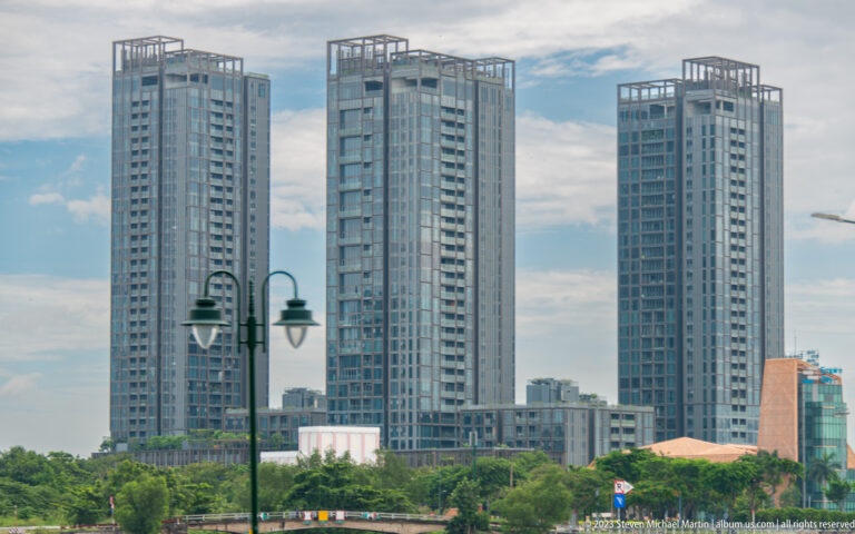 Three modern apartment towers rising above trees and lower city buildings.