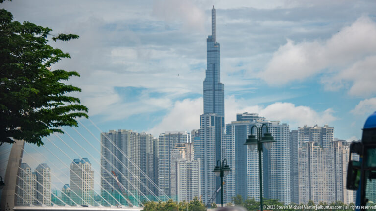 Landmark 81 above dense apartment towers, with bridge cables crossing the foreground.