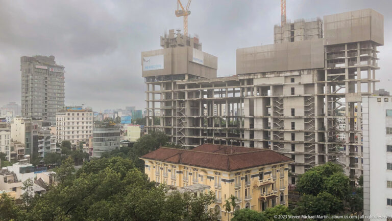 Concrete high-rise under construction behind a yellow historic building with a red tile roof.