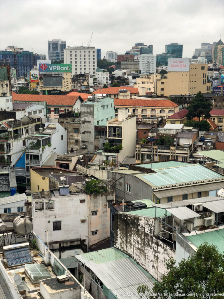 Dense urban rooftops with water tanks, weathered walls, and larger commercial buildings beyond.